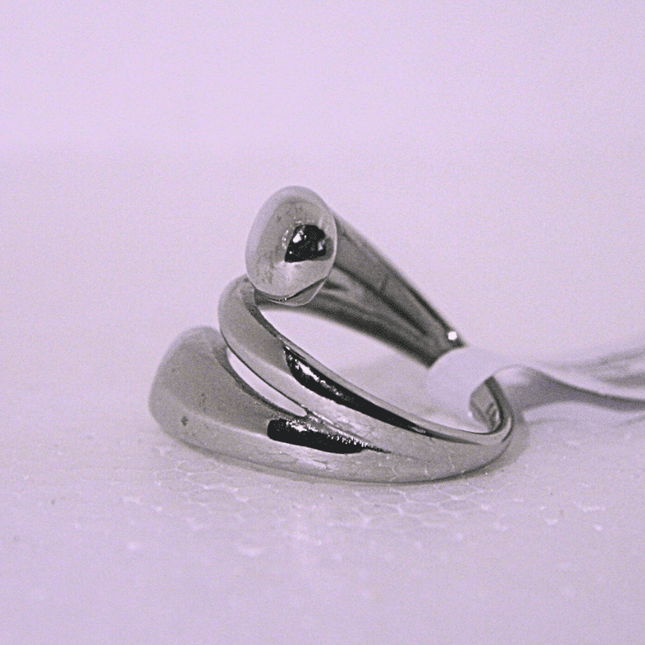 Vista lateral del anillo enrollado moderno plateado, detalle del diseño único y acabado de alta calidad.