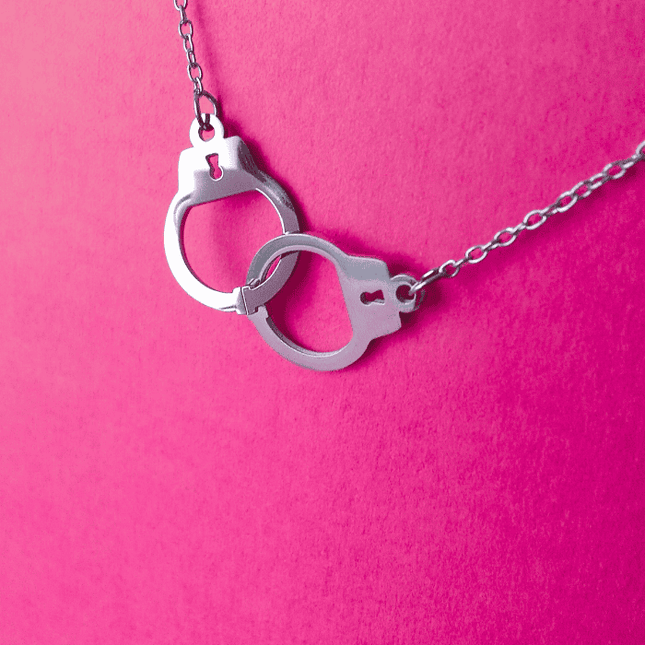 Detalle del colgante en forma de esposas entrelazadas, acabado en plata. Joyería simbólica con actitud rebelde.