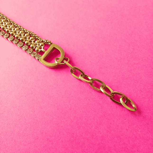 Diseño trenzado y elementos metálicos en pulsera dorada. Volumen visual con carácter.