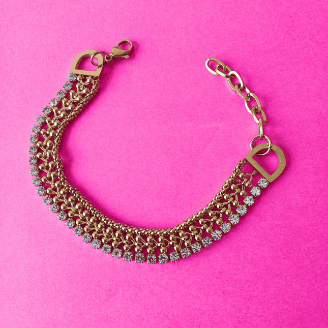 Pulsera dorada de acero inoxidable con tres hileras: circonitas brillantes, trenzado metálico y detalle de cerezas. Estilo audaz y sofisticado.