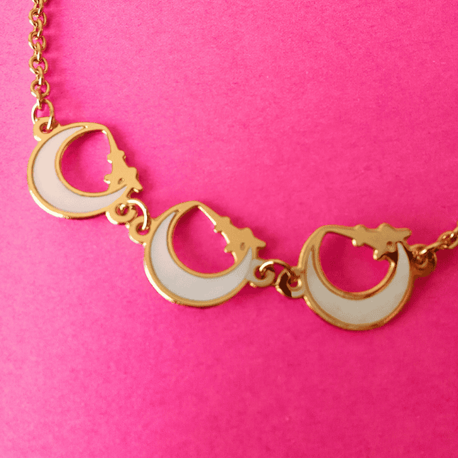 Tres medias lunas con borde dorado colgando de cadena dorada. Estilo místico y con intención.
