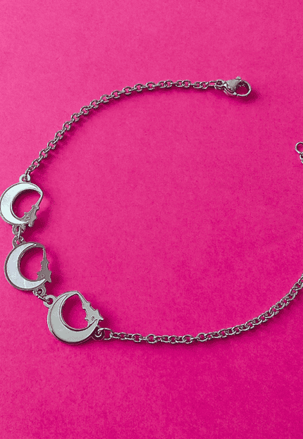 Pulsera plateada de acero inoxidable con tres colgantes de media luna blanca. Diseño místico y elegante.