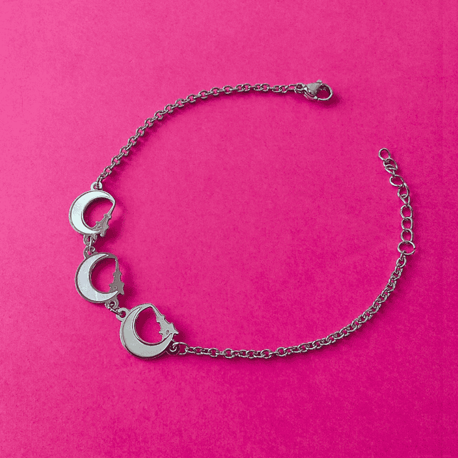 Pulsera plateada de acero inoxidable con tres colgantes de media luna blanca. Diseño místico y elegante.